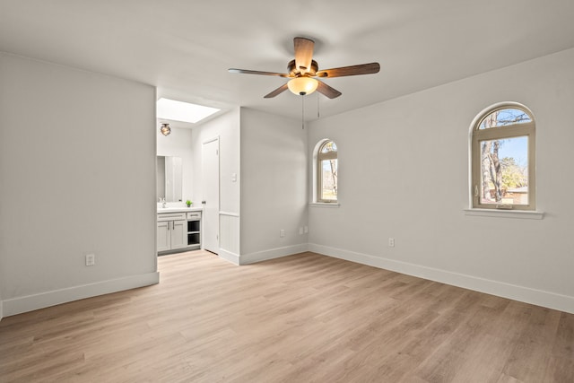 empty room with light wood-type flooring, baseboards, and a skylight