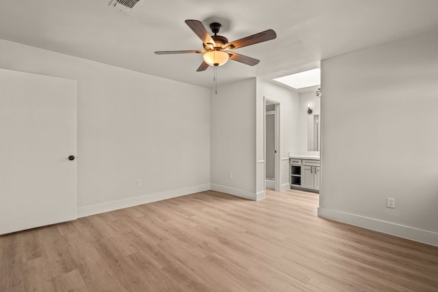 spare room with light wood finished floors, a skylight, baseboards, visible vents, and ceiling fan