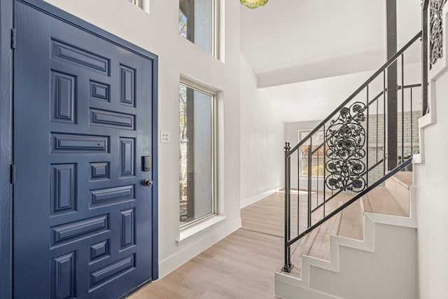 foyer entrance with stairs, wood finished floors, a towering ceiling, and baseboards