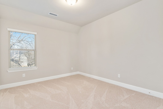 empty room with light carpet, visible vents, baseboards, and lofted ceiling