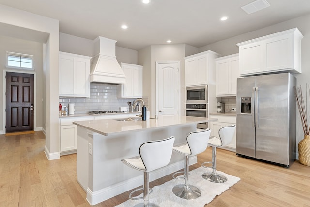 kitchen with stainless steel appliances, light countertops, visible vents, a sink, and premium range hood