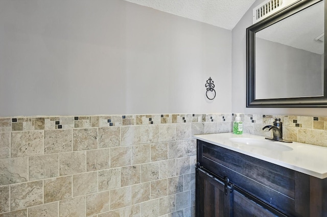 bathroom with a textured ceiling, vanity, and tile walls