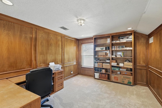 office area featuring wooden walls, light colored carpet, visible vents, and a textured ceiling