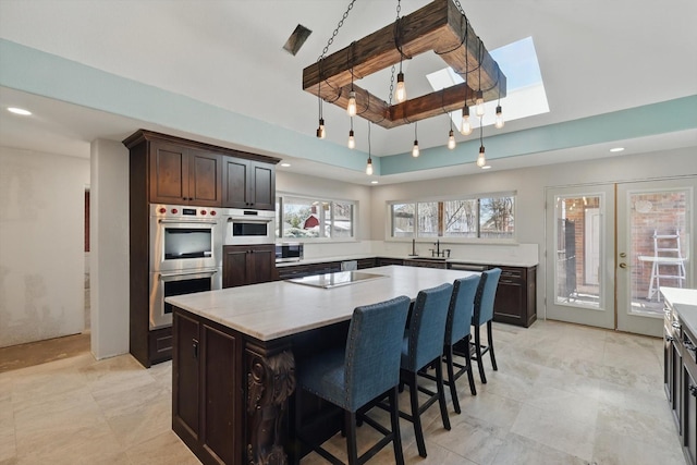 kitchen with dark brown cabinets, a center island, appliances with stainless steel finishes, french doors, and a sink