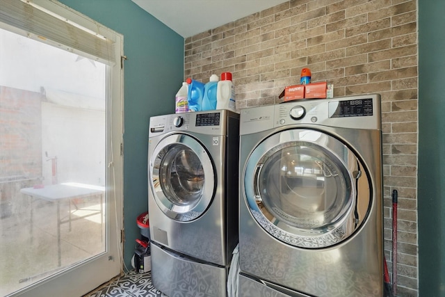 clothes washing area with washing machine and clothes dryer, laundry area, and brick wall