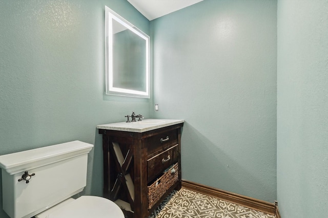 half bath with toilet, baseboards, and vanity