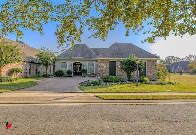 view of front of house with brick siding, driveway, a front lawn, and roof with shingles