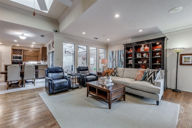 living room featuring a skylight, light wood finished floors, recessed lighting, ornamental molding, and baseboards