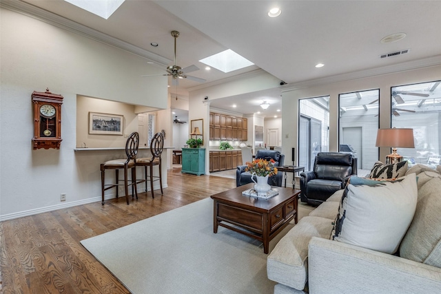 living room featuring a skylight, crown molding, light wood finished floors, a ceiling fan, and baseboards