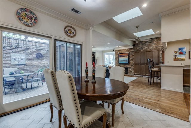 dining area with a skylight, visible vents, a ceiling fan, crown molding, and a brick fireplace