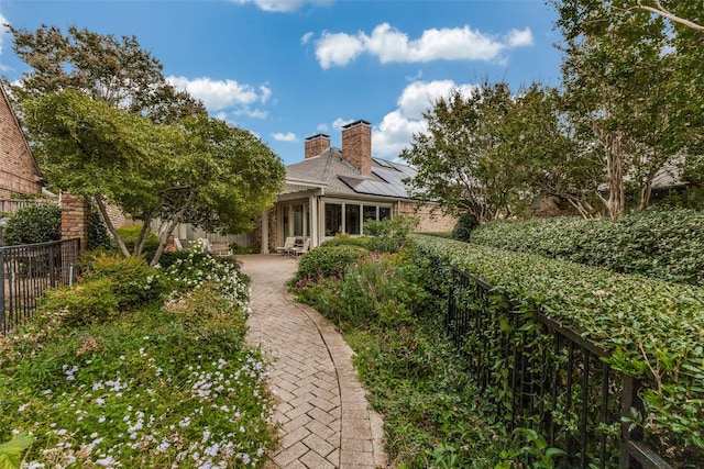 view of front of home with roof mounted solar panels, a fenced backyard, a patio, and a chimney