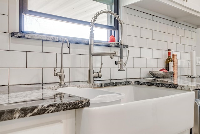 kitchen with dark stone counters, a sink, and backsplash