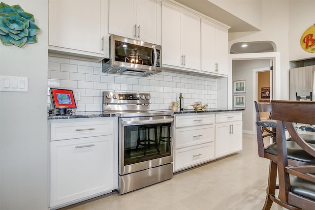 kitchen featuring tasteful backsplash, white cabinetry, stainless steel appliances, and dark stone counters