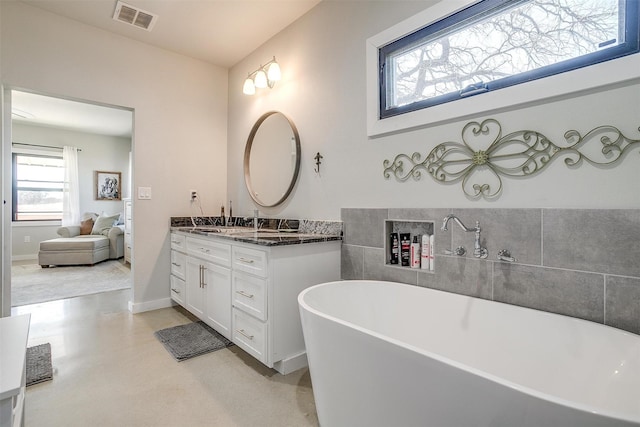 bathroom featuring baseboards, visible vents, concrete flooring, vanity, and a freestanding tub