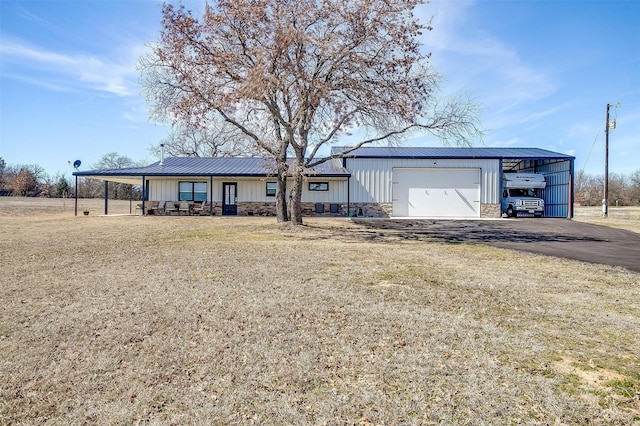 view of front of property featuring metal roof, a garage, driveway, stone siding, and board and batten siding