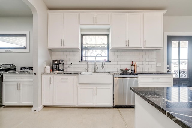 kitchen featuring a sink, white cabinetry, stainless steel dishwasher, backsplash, and dark stone counters