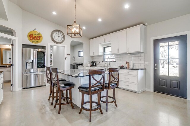 kitchen with stainless steel refrigerator with ice dispenser, decorative backsplash, a kitchen island, concrete flooring, and a kitchen breakfast bar