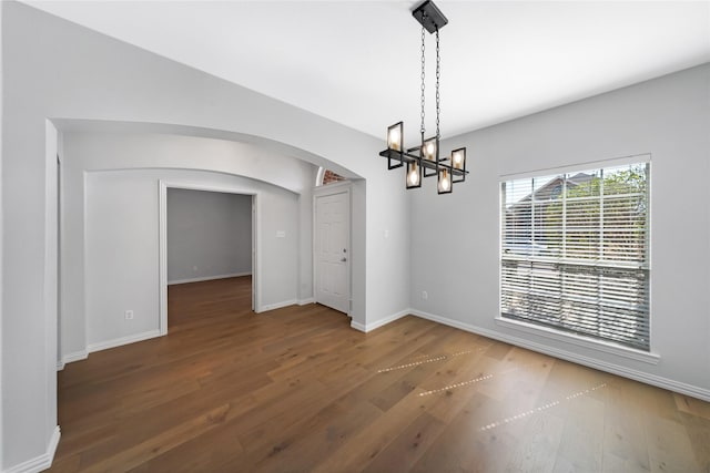 unfurnished dining area with a chandelier, arched walkways, baseboards, and wood finished floors