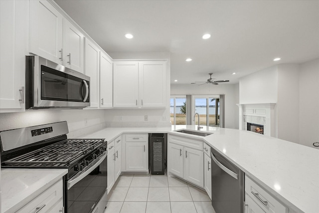 kitchen with recessed lighting, a fireplace, a sink, white cabinets, and appliances with stainless steel finishes