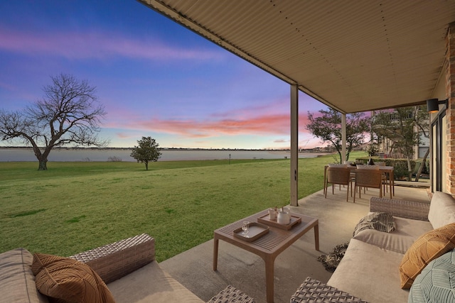 patio terrace at dusk featuring outdoor dining area, a lawn, a water view, and an outdoor living space