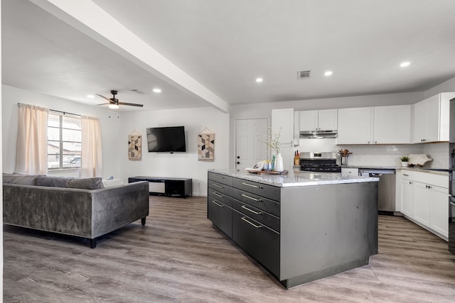 kitchen with under cabinet range hood, stainless steel appliances, a kitchen island, white cabinetry, and visible vents