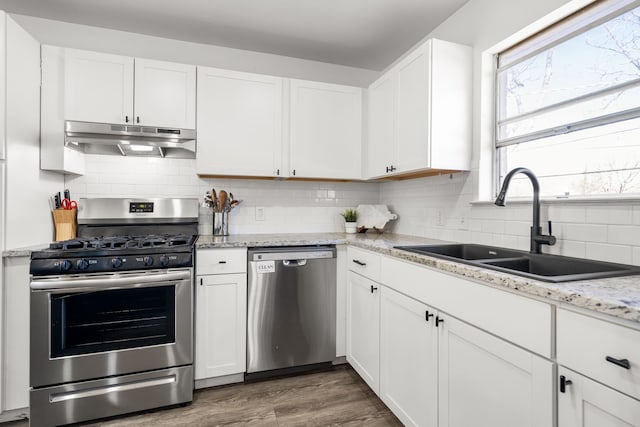 kitchen featuring stainless steel appliances, decorative backsplash, white cabinets, a sink, and under cabinet range hood