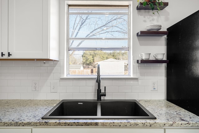 kitchen with decorative backsplash, light stone countertops, white cabinetry, open shelves, and a sink