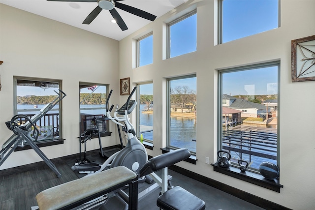 workout room featuring a water view, ceiling fan, a high ceiling, and baseboards