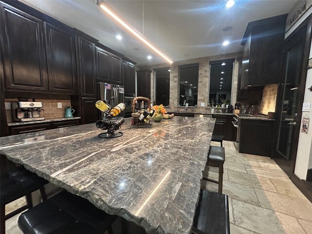 kitchen featuring dark cabinets, a breakfast bar, backsplash, a center island, and stone tile flooring