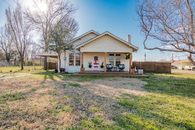 back of property featuring covered porch, a chimney, fence, and a lawn