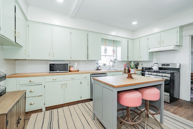 kitchen with under cabinet range hood, butcher block counters, appliances with stainless steel finishes, light wood-type flooring, and decorative backsplash