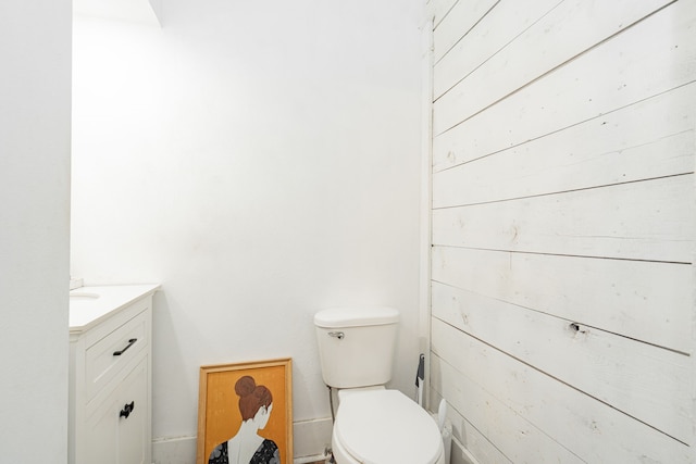 bathroom with toilet, wooden walls, and vanity