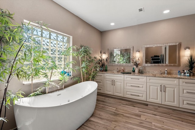 full bath featuring wood finished floors, a sink, a freestanding tub, double vanity, and visible vents