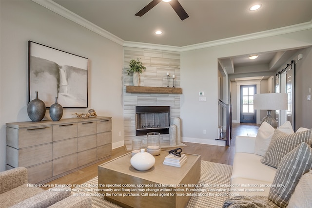 living room with a fireplace, crown molding, light wood-style flooring, a barn door, and a ceiling fan