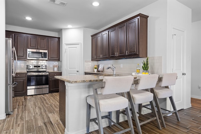 kitchen featuring visible vents, appliances with stainless steel finishes, a peninsula, dark brown cabinets, and light wood-style floors