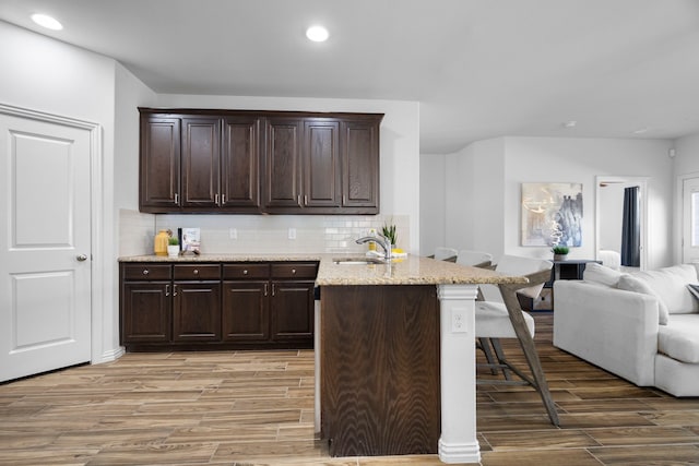 kitchen with dark brown cabinetry, light wood-style flooring, open floor plan, a kitchen bar, and a sink