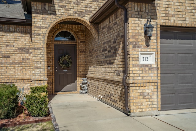 entrance to property with an attached garage, roof with shingles, and brick siding