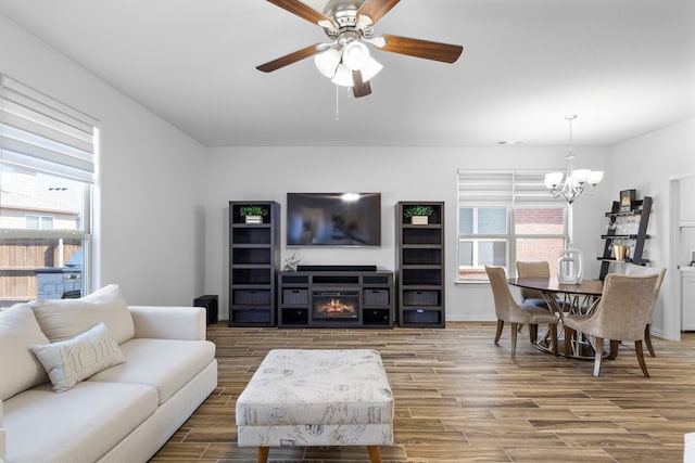 living room featuring wood finish floors, a lit fireplace, baseboards, and ceiling fan with notable chandelier