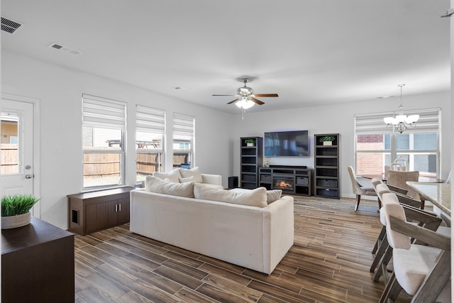 living room featuring wood tiled floor, visible vents, a glass covered fireplace, and ceiling fan with notable chandelier