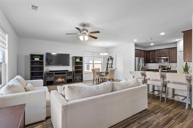 living area with ceiling fan with notable chandelier, visible vents, and wood finish floors