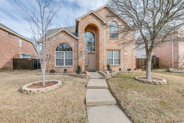 traditional home featuring fence, a front lawn, and brick siding