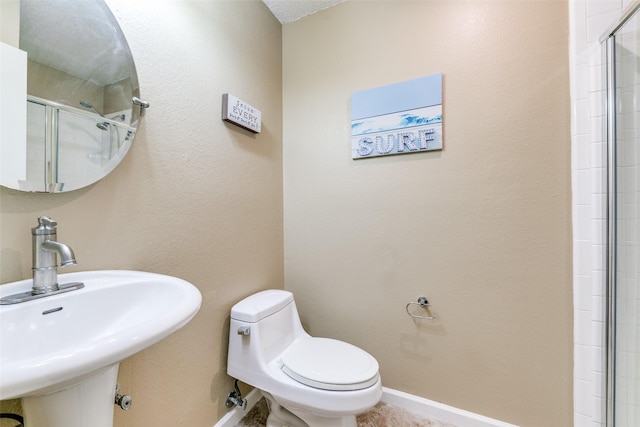 full bath with tiled shower, a sink, toilet, and baseboards