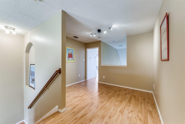 empty room featuring light wood-style floors, baseboards, visible vents, and a textured ceiling