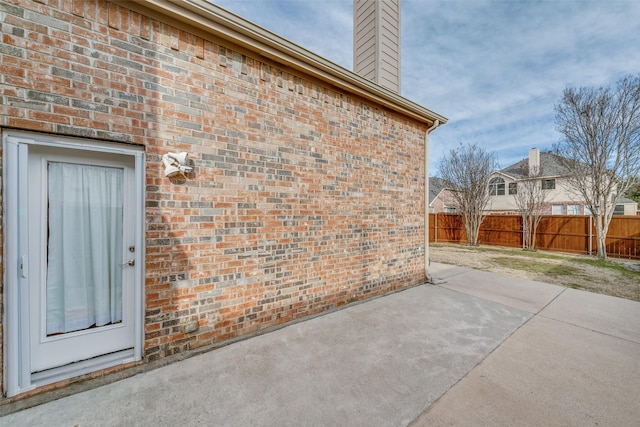 exterior space featuring brick siding, fence, a chimney, and a patio