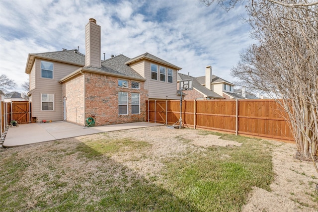 back of property with a fenced backyard, brick siding, a yard, a chimney, and a patio area