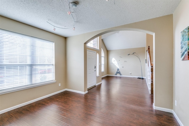 foyer entrance featuring arched walkways, vaulted ceiling, a wealth of natural light, and wood finished floors