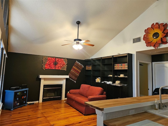 living room with ceiling fan, visible vents, wood finished floors, and a glass covered fireplace