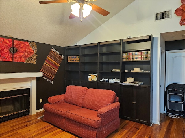 living area featuring a glass covered fireplace, visible vents, vaulted ceiling, and wood finished floors