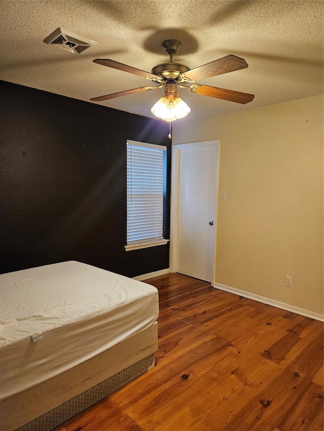 unfurnished bedroom featuring baseboards, visible vents, a ceiling fan, wood finished floors, and a textured ceiling