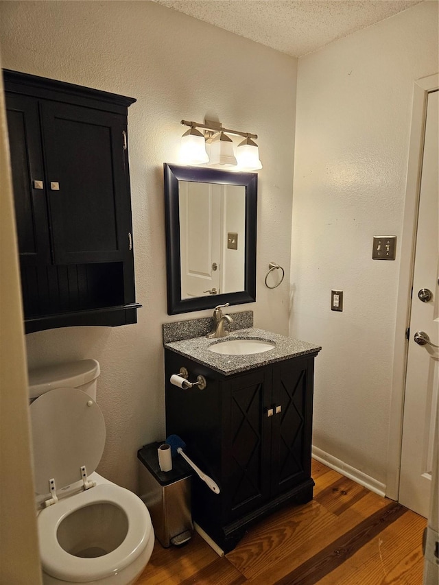 bathroom with a textured ceiling, toilet, wood finished floors, and vanity